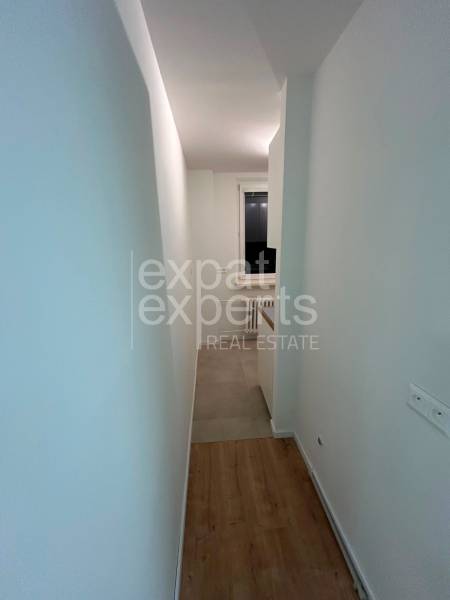 A narrow long corridor in a 2-room apartment, light walls, wooden floor.