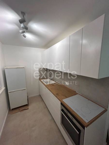 Kitchen unit with a cooktop and oven in a 2-room apartment, simple white design.