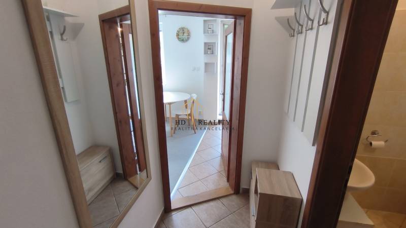 Hallway of a 2-room apartment with coat hooks, a mirror, and a view of the dining area.