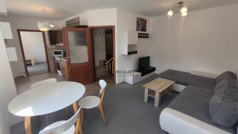 Living room of a two-room apartment with a sofa set, dining table, and kitchenette.