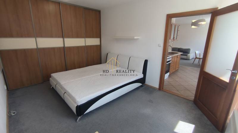 Bedroom with a large wardrobe and a double bed, next to a living room with a kitchen unit.