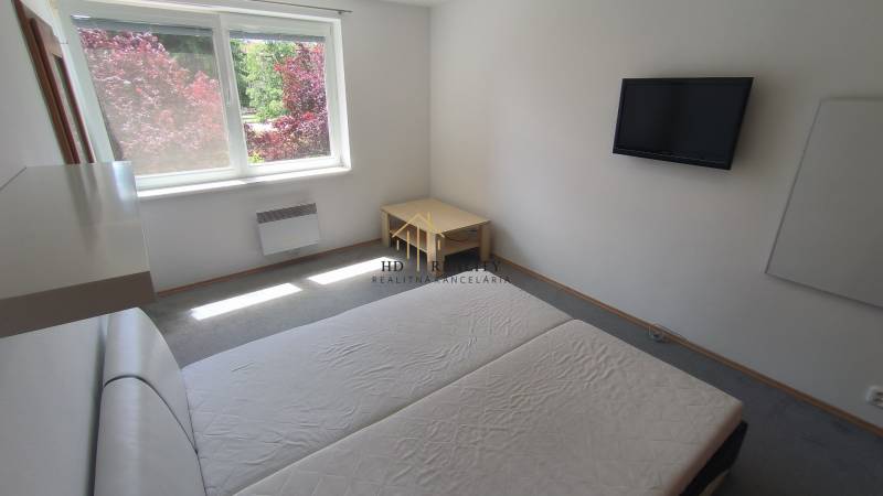 Bedroom in a 2-room apartment with a TV, bed, and garden view.
