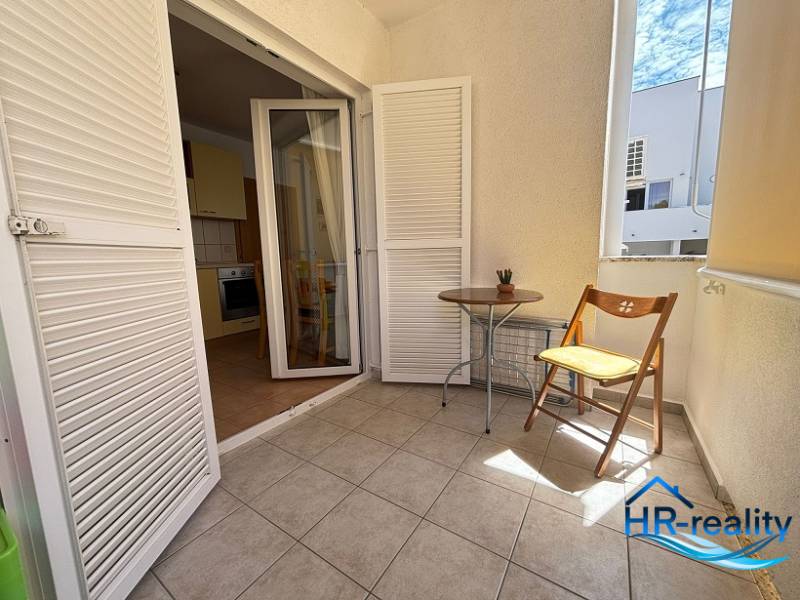 A balcony in a 2-room apartment with white blinds and a wooden chair.