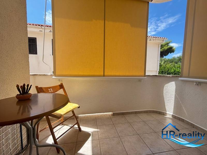 Balcony of a 2-room apartment in Novalja with a wooden table and a green view.