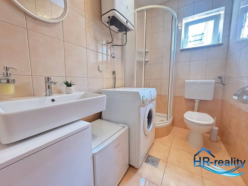 Bathroom in a 2-room apartment with a washing machine, shower, and toilet.