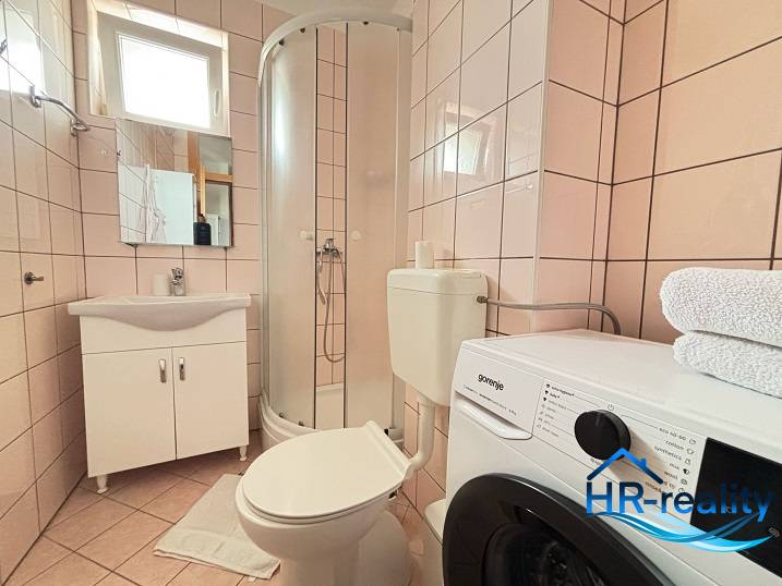 A bathroom in a 3-room apartment with a toilet, shower, and washing machine.