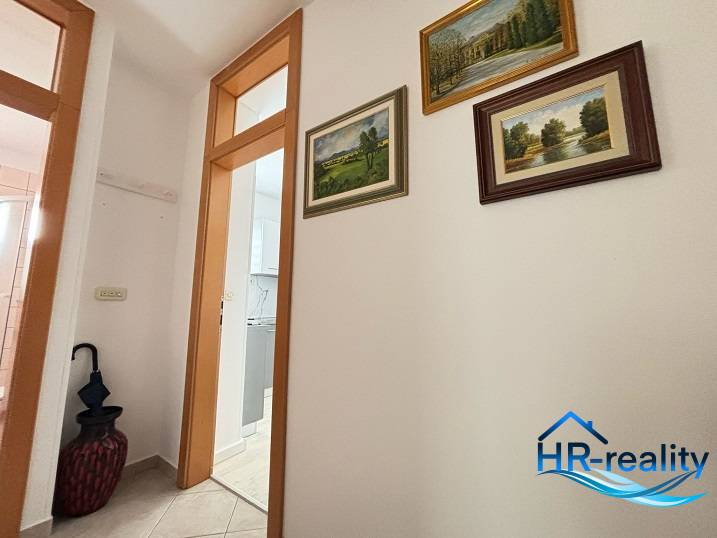 Hallway of a 3-room apartment with paintings on the wall and a door to the bathroom.