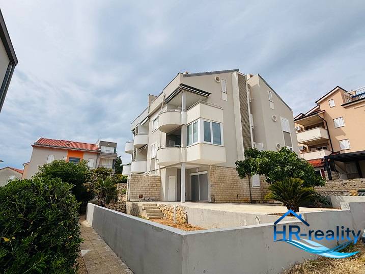 Apartment building with balconies in Novalja, 3-bedroom apartments, surrounded by greenery and shrubs.