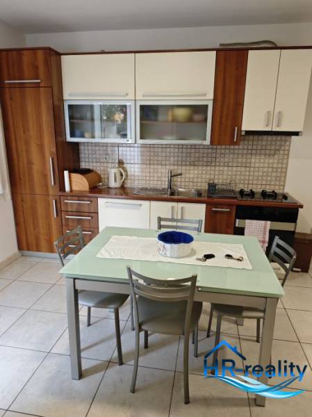 A kitchen in a 2-room apartment with wooden cabinets and a dining table with four chairs.