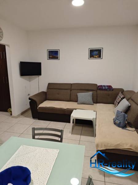 Living room in a two-room apartment with a sofa, a table, and a TV on the wall.