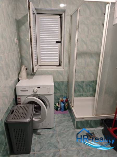 A bathroom in a two-room apartment with a washing machine, shower, and window.