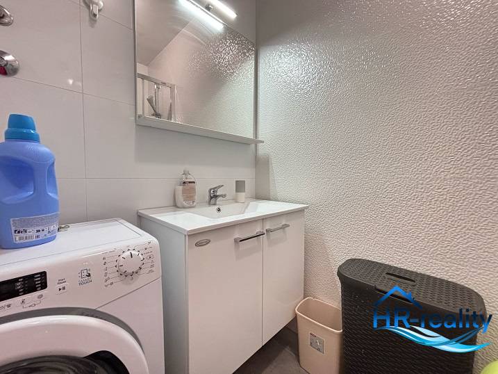 Bathroom in a 2-room apartment with a washing machine, sink, and storage space.