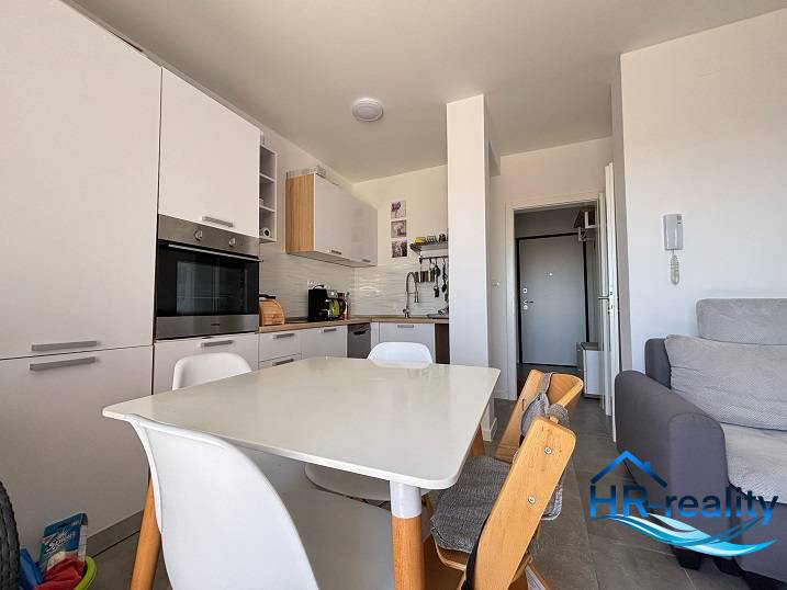 A kitchen in a 2-room apartment with white appliances and a wooden dining table.