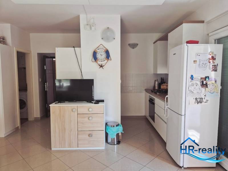 A kitchen in a 2-room apartment with appliances, a wardrobe, a television, and wall decorations.