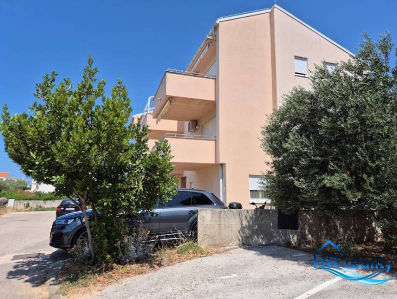 A building with a parking lot and trees near a 2-room apartment in Novalja.