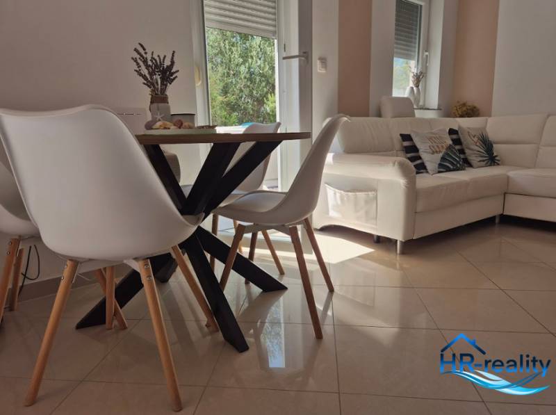 Interior of a 2-room apartment with a wooden table, white chairs, and a comfortable couch.