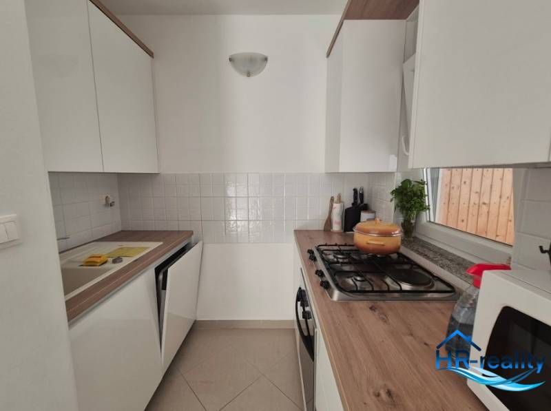 Kitchen in a 2-room apartment, light cabinets, stove, microwave, wooden countertop.