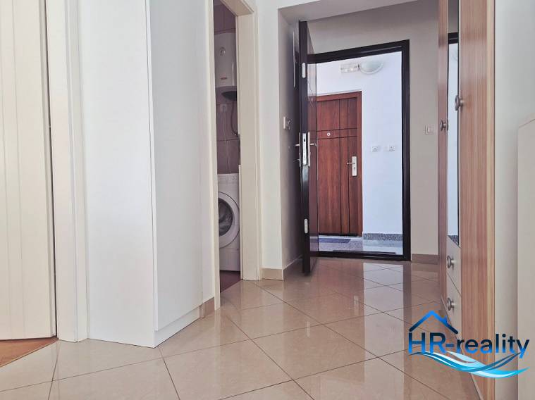 A hallway in a 2-room apartment with a washing machine and entrance door.