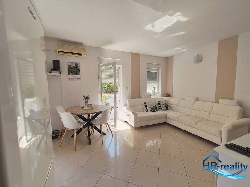 A bright living room in a two-room apartment with a white sofa and a dining table.