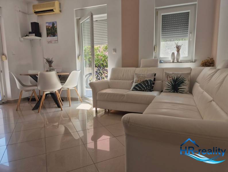A bright living room in a two-room apartment with a white sofa and a dining table.