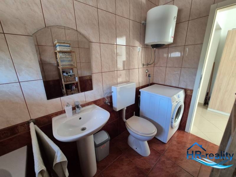 A bathroom with a mirror, sink, washing machine, and toilet in a 2-room apartment.