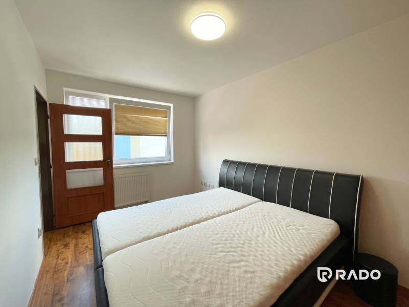 A bedroom with a double bed, a door, and a large window in a two-room apartment.