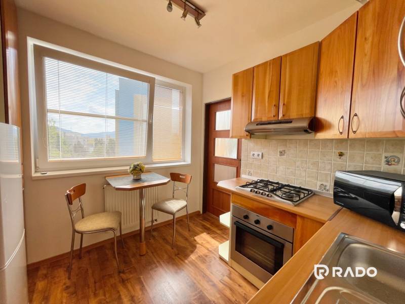 A kitchen with a stove, microwave, and a table with two chairs in a two-room apartment.
