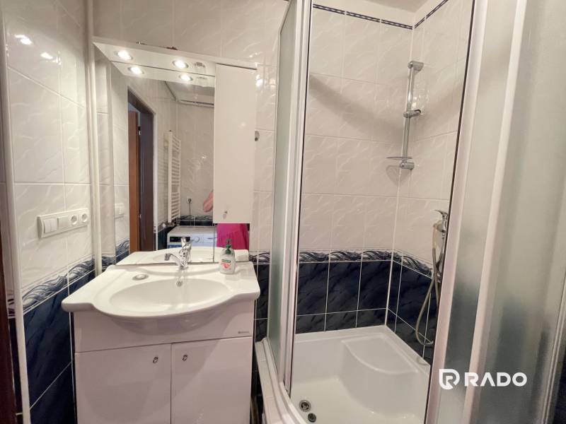 Bathroom in a 2-room apartment with a sink, shower, and mirror above the cabinet.