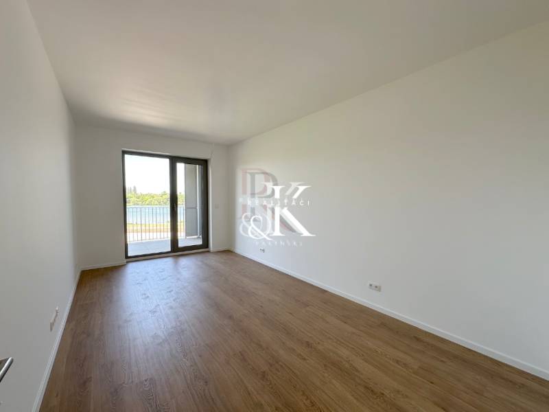 A spacious room in a 2-room apartment with wooden flooring and a French window.