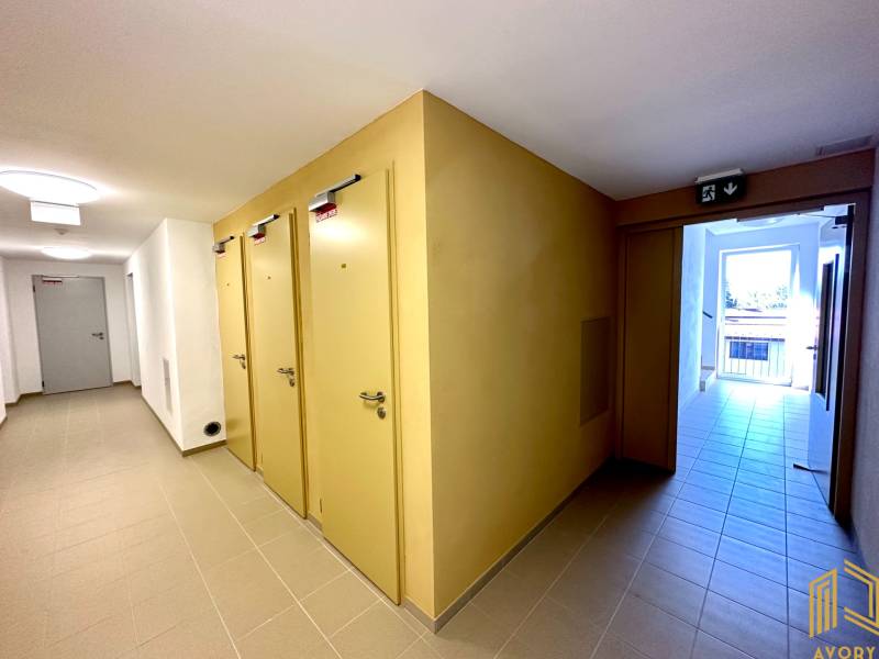 A hallway with multiple doors in a 2-room apartment, light-colored tiles, and an emergency exit.