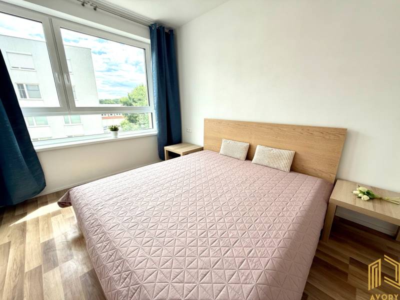 A bright bedroom with a large window and a wooden bed in a two-room apartment.