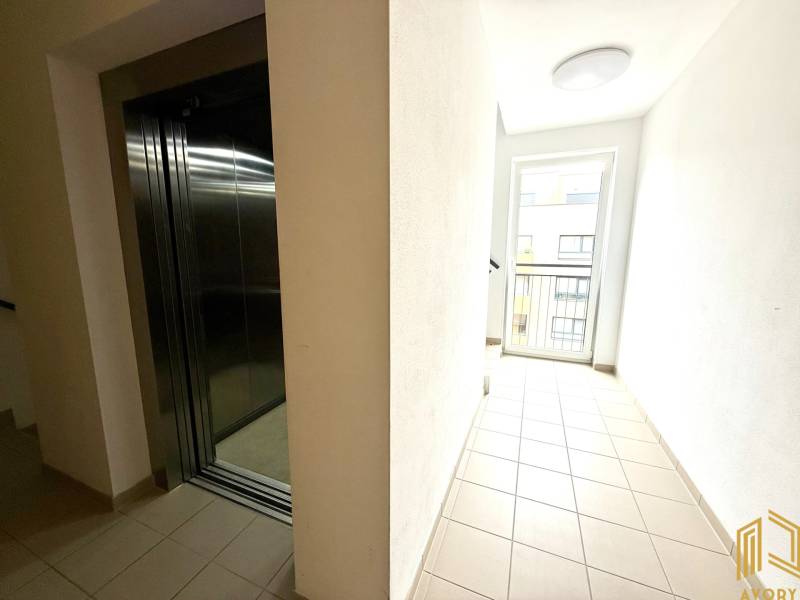 A hallway with light paneling and an elevator in a 2-room apartment.