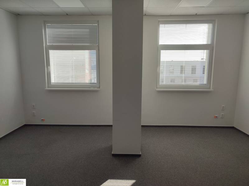 White offices with two windows and a pillar, smooth walls, unobtrusive carpet.