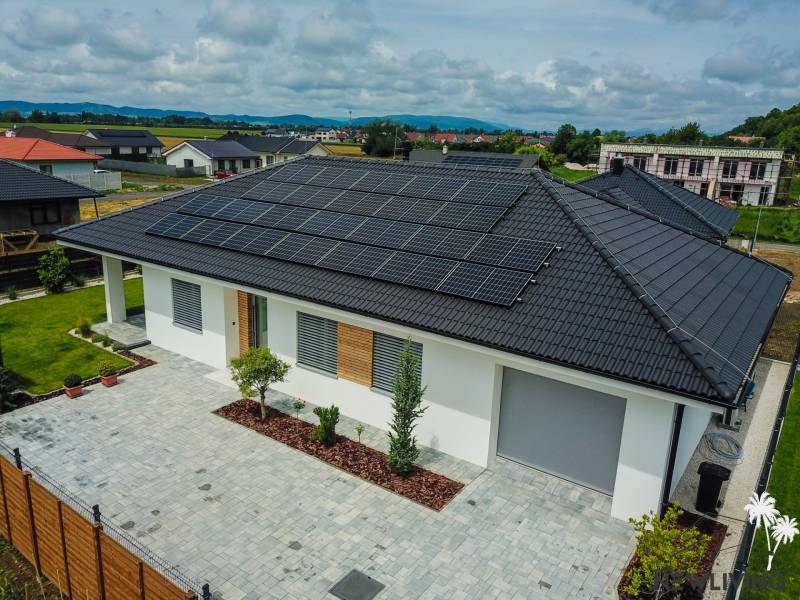 A family house in Piešťany with photovoltaic panels on the roof is surrounded by a green garden.
