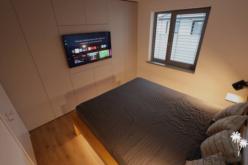 A bedroom in a family house with a TV, a large bed, and a window.