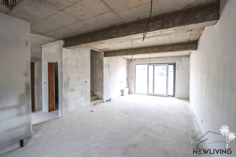 A bright room in a family house with a concrete ceiling, stairs, and glass doors.