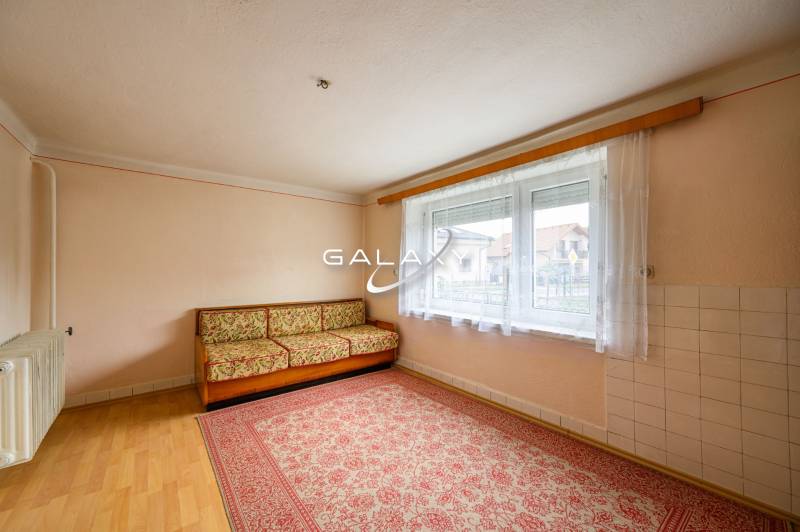 A room in a family house with a carpet, a couch, and a large window.