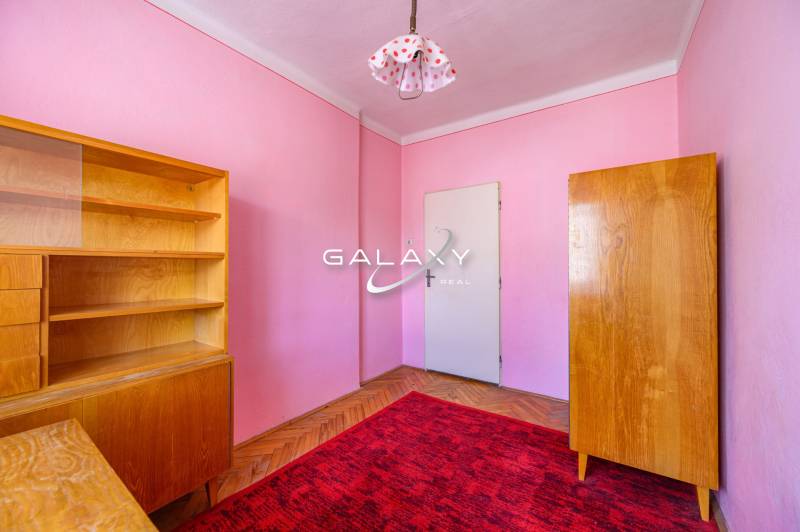 A room in a family house with wooden furniture, a red carpet, and pink walls.