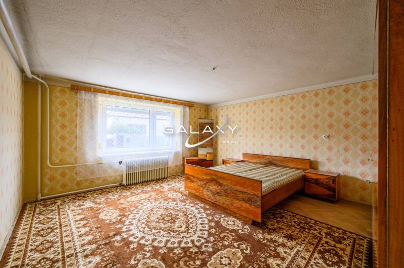 Bedroom with a bed, patterned wallpaper, and carpets in a family house.