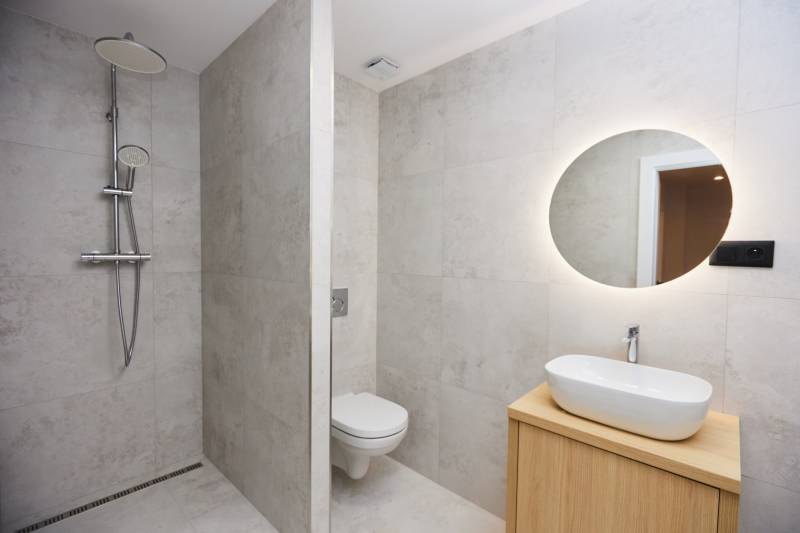 Bathroom in a 2-room apartment with an open shower and illuminated mirror.