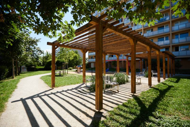 A wooden pergola with benches in a park in Košice, Juh district, surrounded by greenery.
