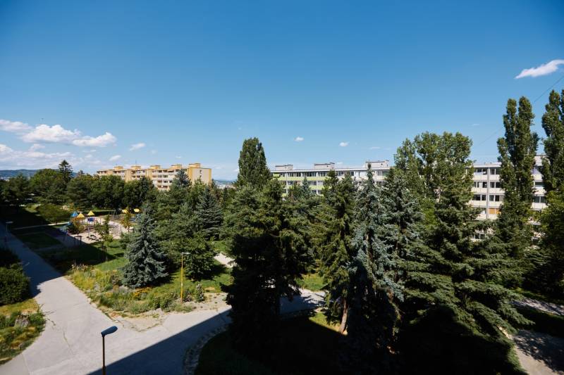 A view of apartment buildings surrounded by trees and a playground in Košice, Juh district.