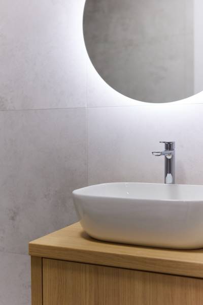 Bathroom with a sink on a wooden cabinet and an illuminated round mirror in a two-room apartment.