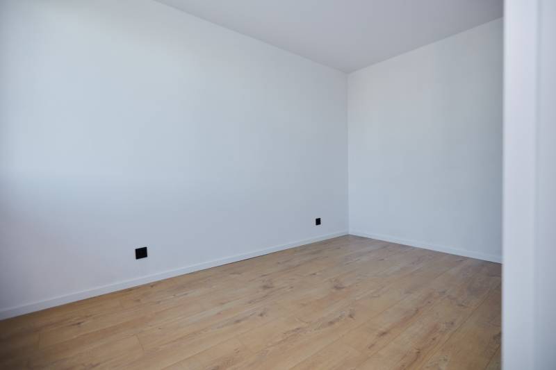 An empty room with white walls and wooden flooring in a two-room apartment.