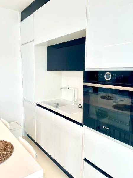 A kitchen in a 2-room apartment with a minimalist white unit and a built-in oven.