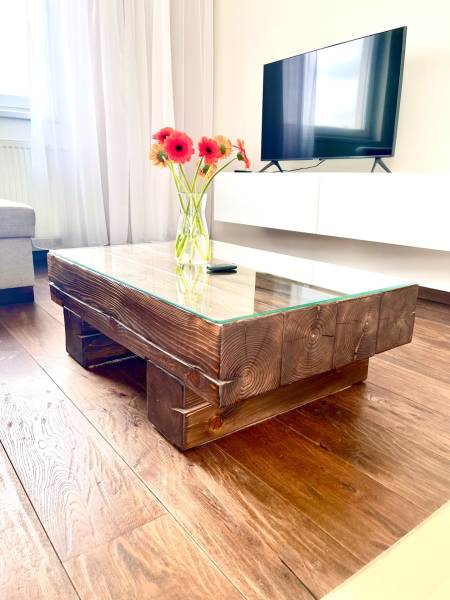 Glass table with a wooden frame and flowers in a vase in a 2-room apartment.