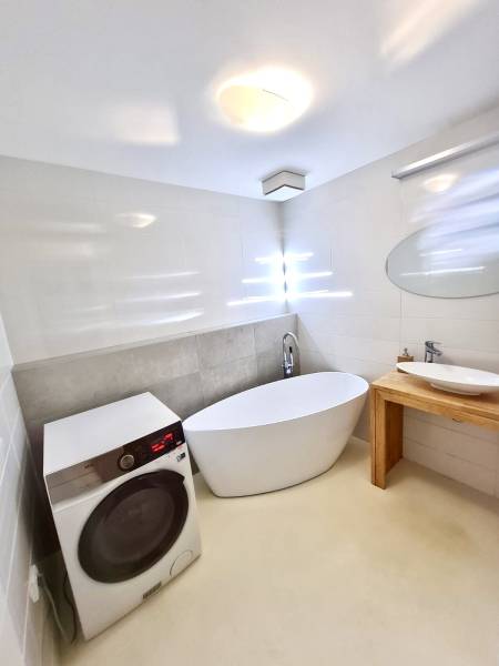 A bathroom in a 2-room apartment with a bathtub, sink, washing machine, and round mirror.