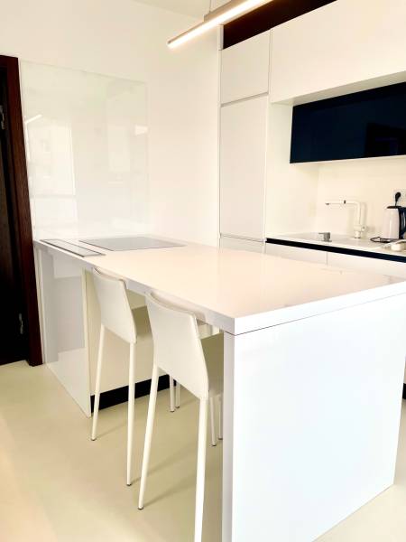 A kitchen in a 2-room apartment with white furniture and a bar counter with stools.