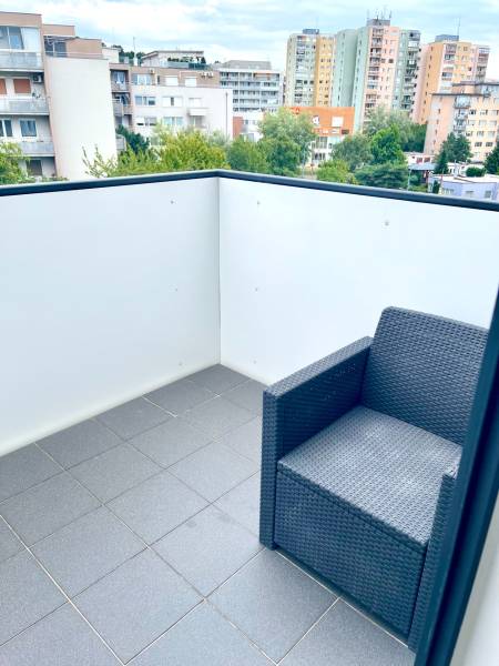 A balcony of a 2-room apartment with a rattan chair and a view of the surrounding apartment buildings.