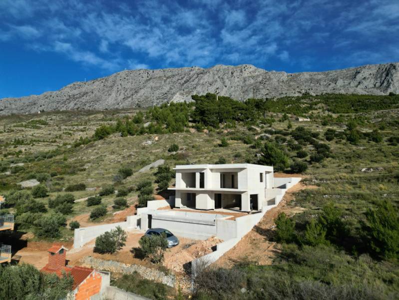 A villa in Duće surrounded by greenery and mountains with a blue sky in the background.
